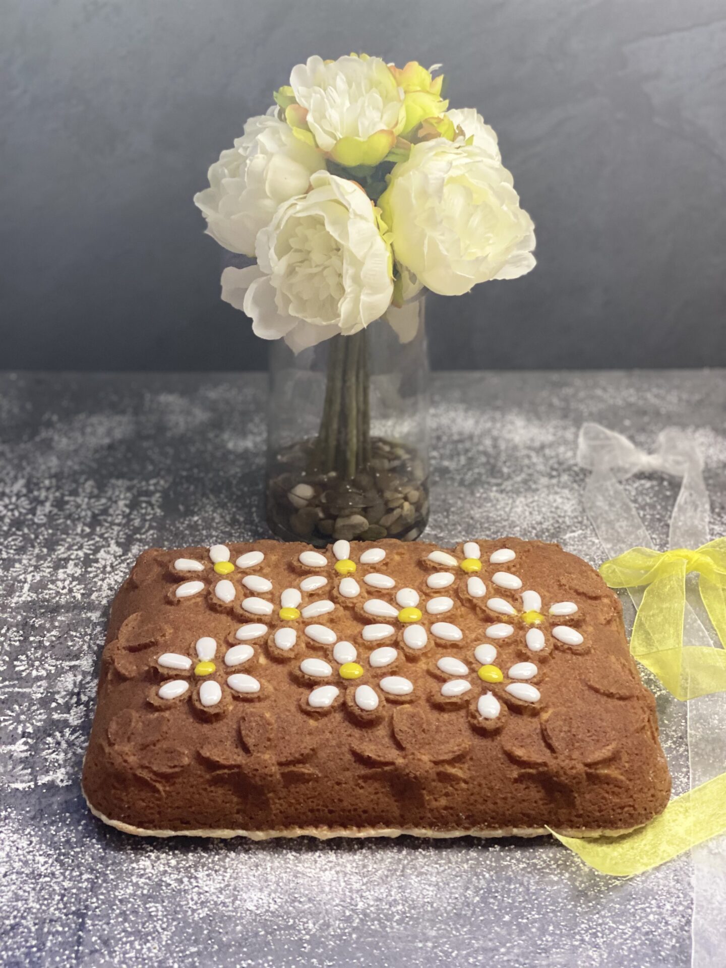 A chocolate cake with flowers design and a vase of plastic flowers