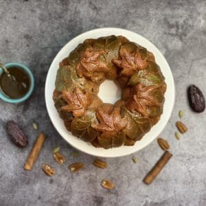 A chocolate bunt cake and pieces of chocolates, raisins, and peanuts on its background