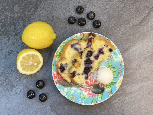 A slice of cake in a floral plate with lemons and blueberries on its side