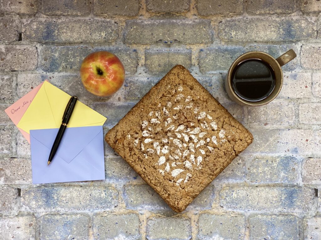 A cake with an apple, a cup of coffee, two colored envelopes, a pink letter, and a pen