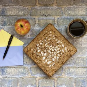 A cake with an apple, a cup of coffee, two colored envelopes, a pink letter, and a pen