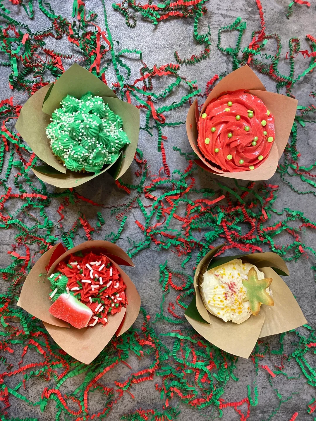 Four cupcakes with different designs and toppings wrapped in brown papers